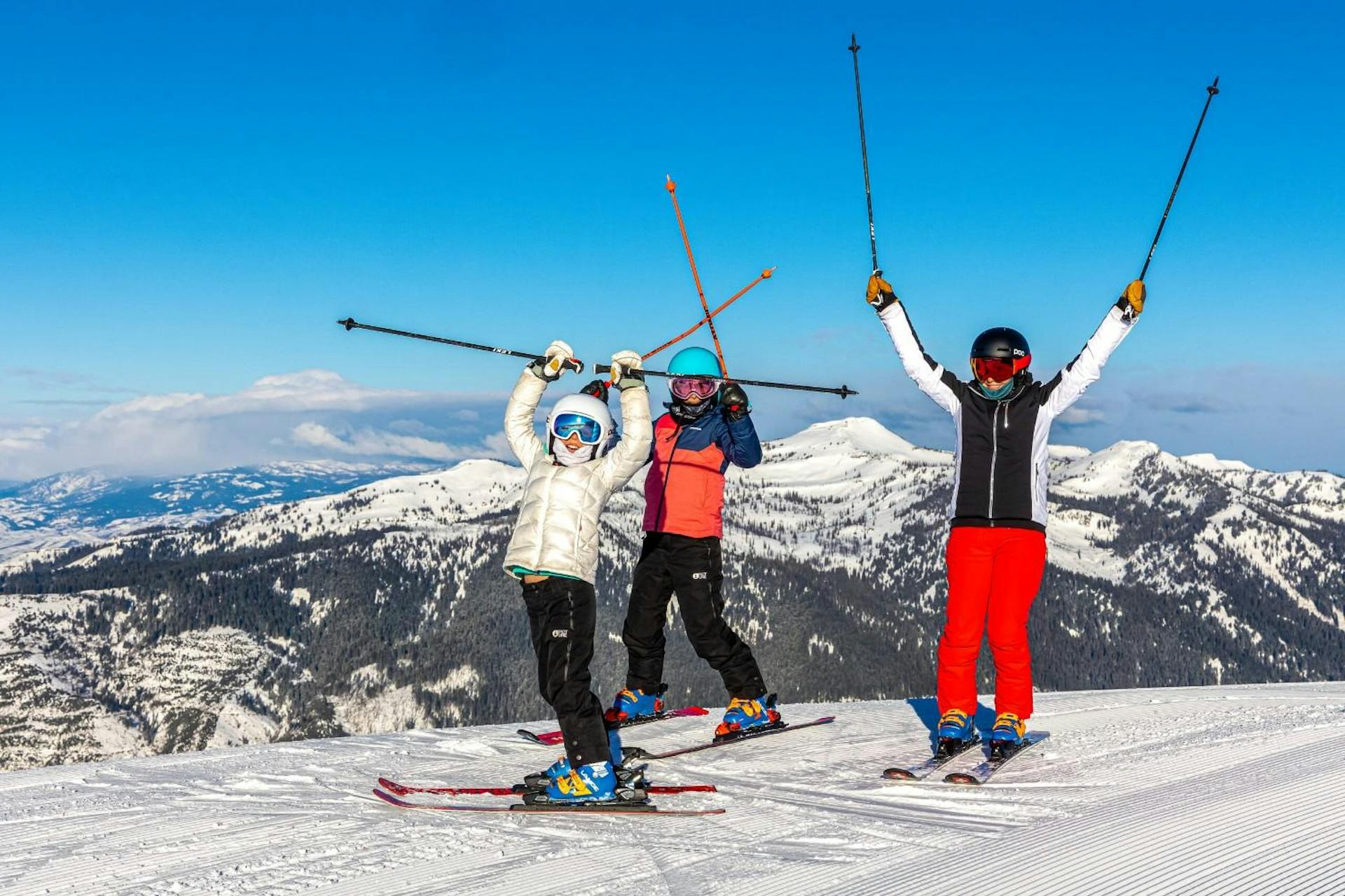 Three skiers of undiscernible gender in orange, white and black ski attire hitting the slopes at Tamarack Resort in Idaho, USA.