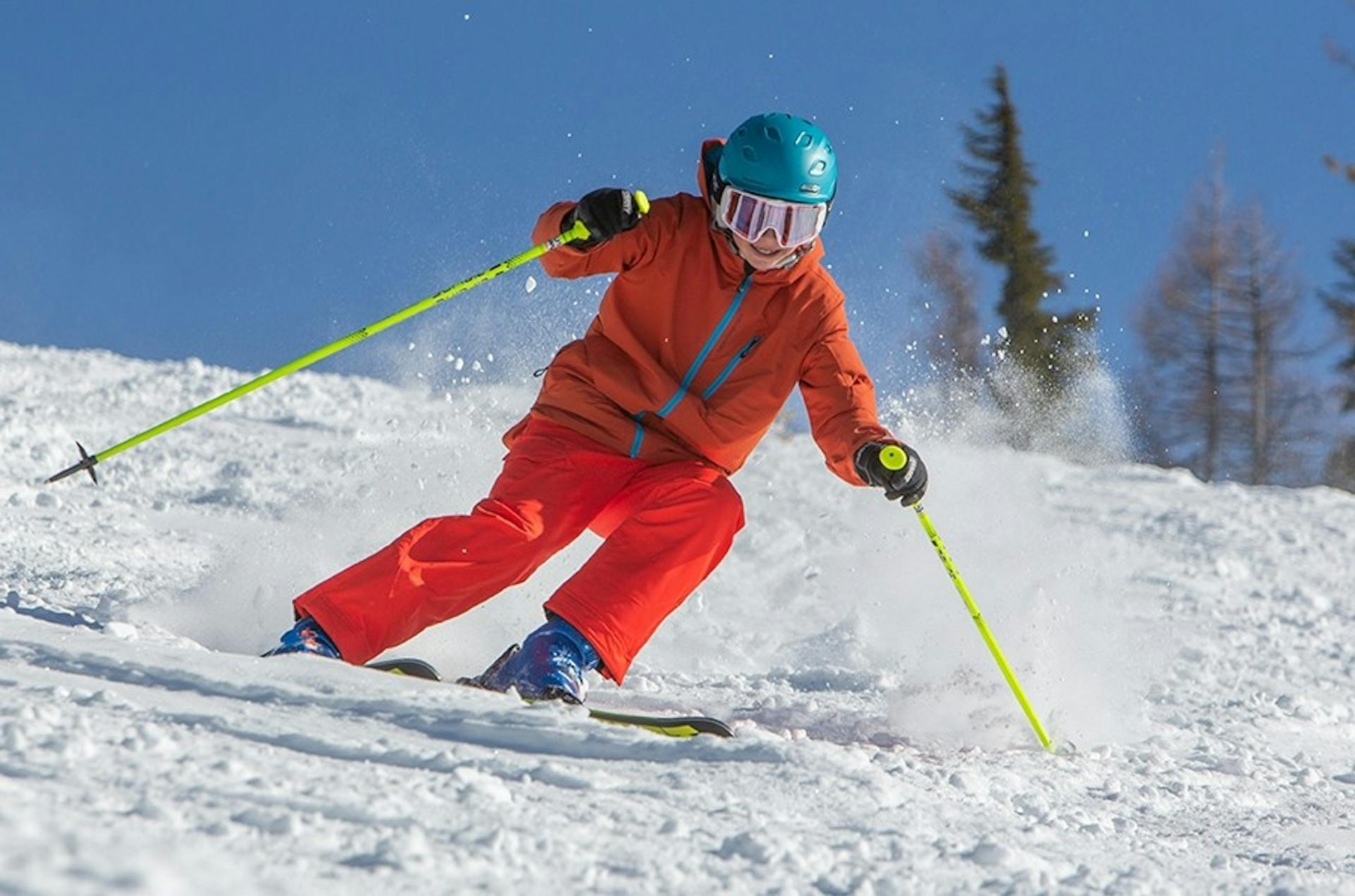 Young skier of undiscernible gender in red ski pants and orange ski jacket hitting the slopes at Silver Mountain in Idaho, USA.