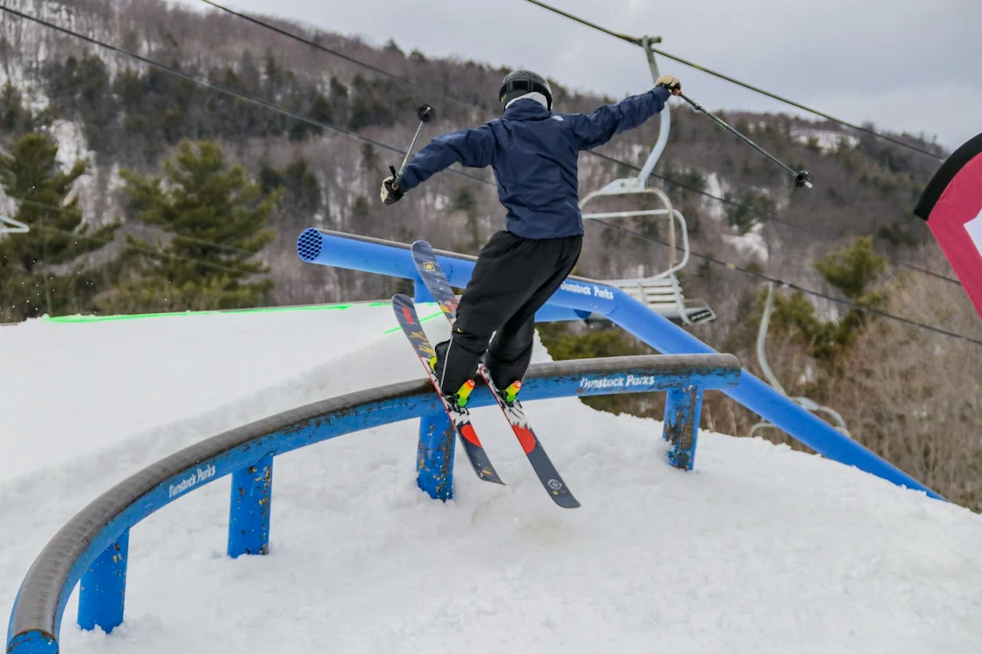 Skier of undiscernible gender in dark blue ski jacket and black ski pants hitting the terrain park at Gunstock Mountain near Boston, Massachusetts, in New Hampshire, USA.
