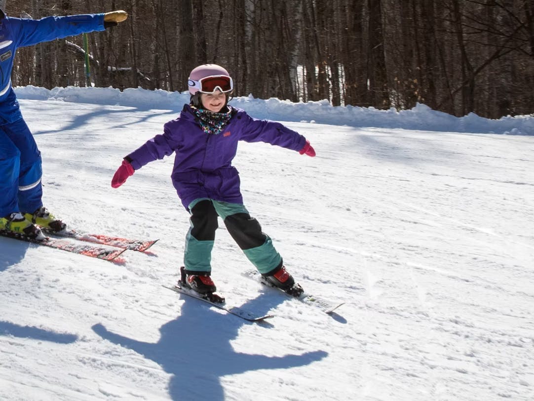 Skier of undiscernible gender in purple ski jacket and teal and black ski pants hitting the slopes at Mount Sunapee near Boston, Massachusetts, in New Hampshire, USA.
