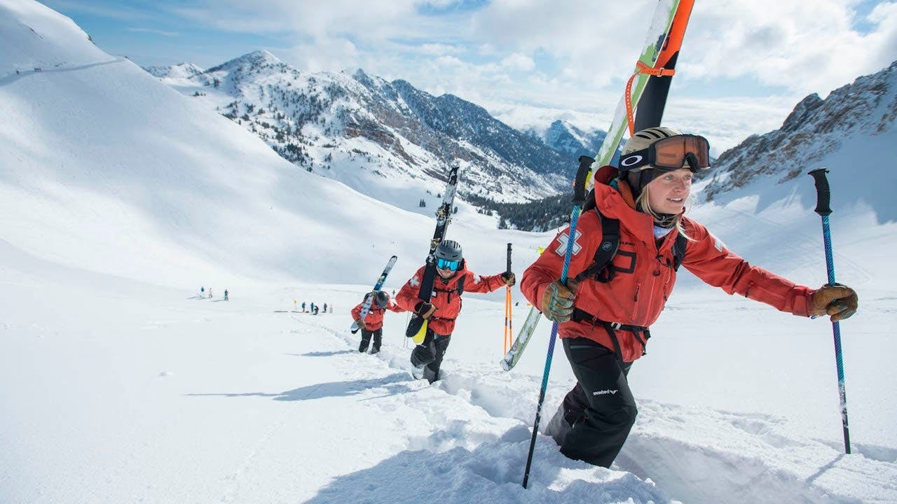 Team of skiers in matching orange ski jackets uphilling at Snowbird near Salt Lake City in Utah, USA.