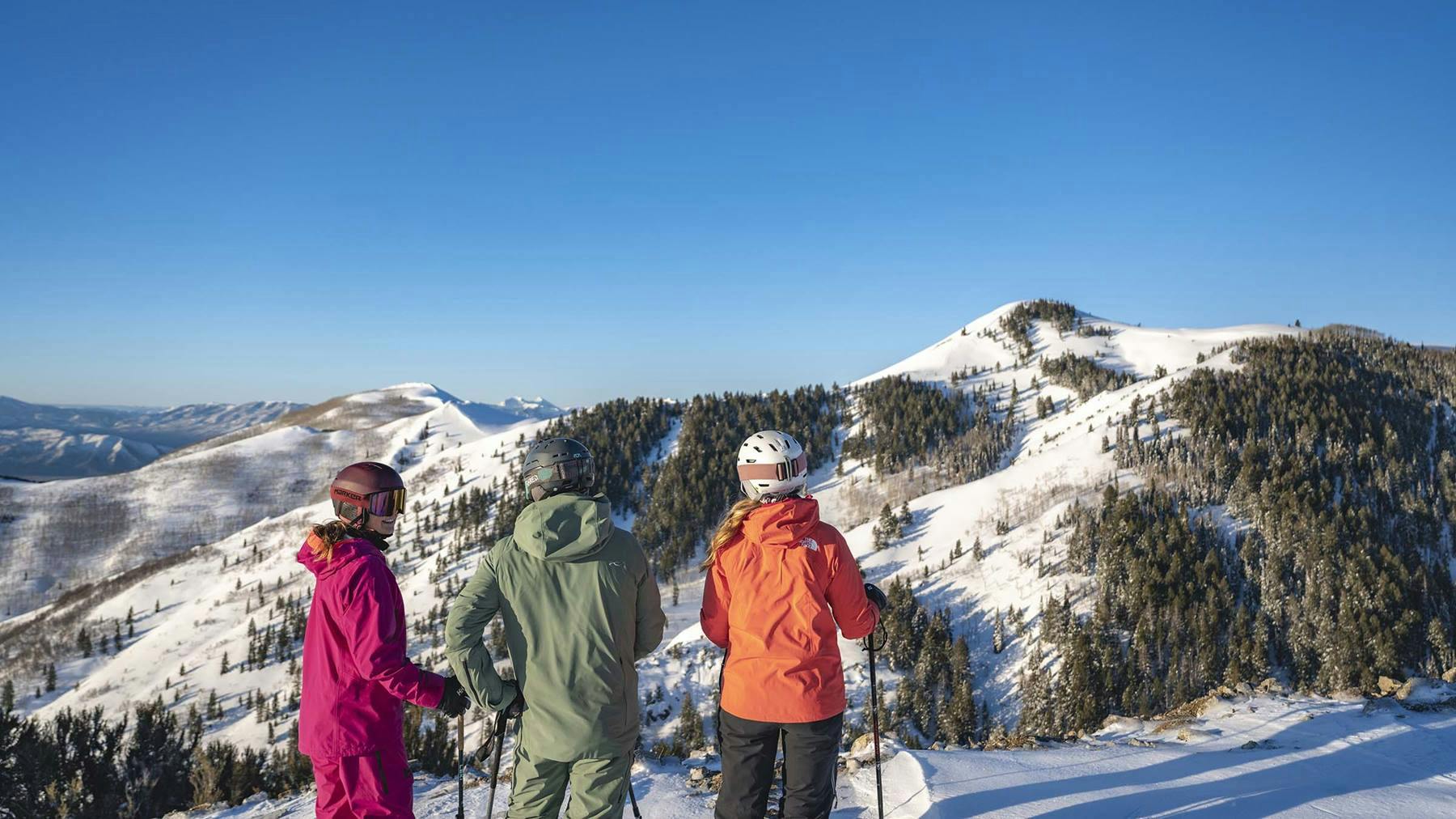 Three skiers in colorful ski attire taking in the views at Deer Valley Resort near Salt Lake City in Utah, USA.