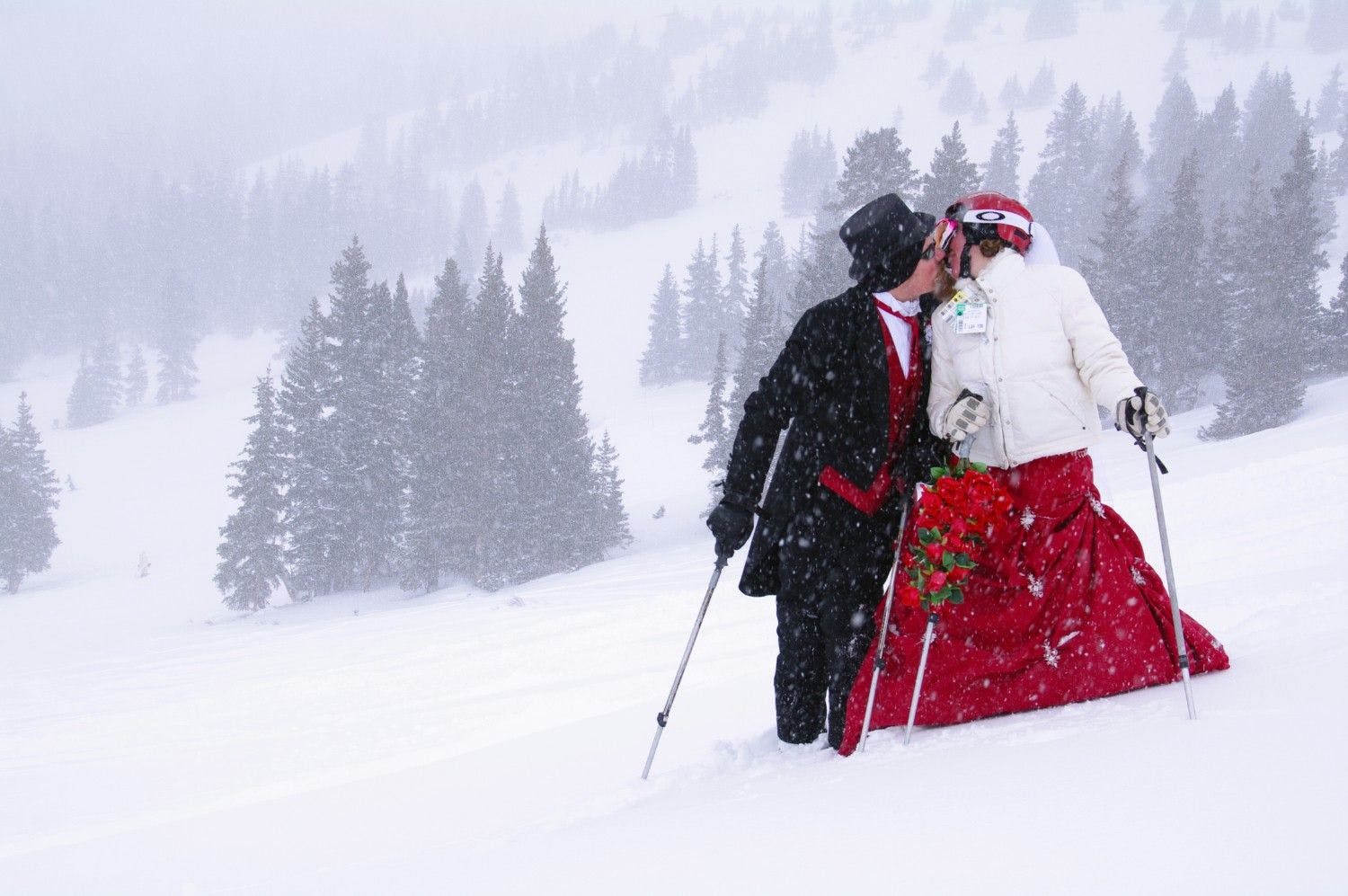Male and female skiers dressed in formal wedding attire sharing a kiss on the slopes of Loveland near Denver in Colorado, USA.