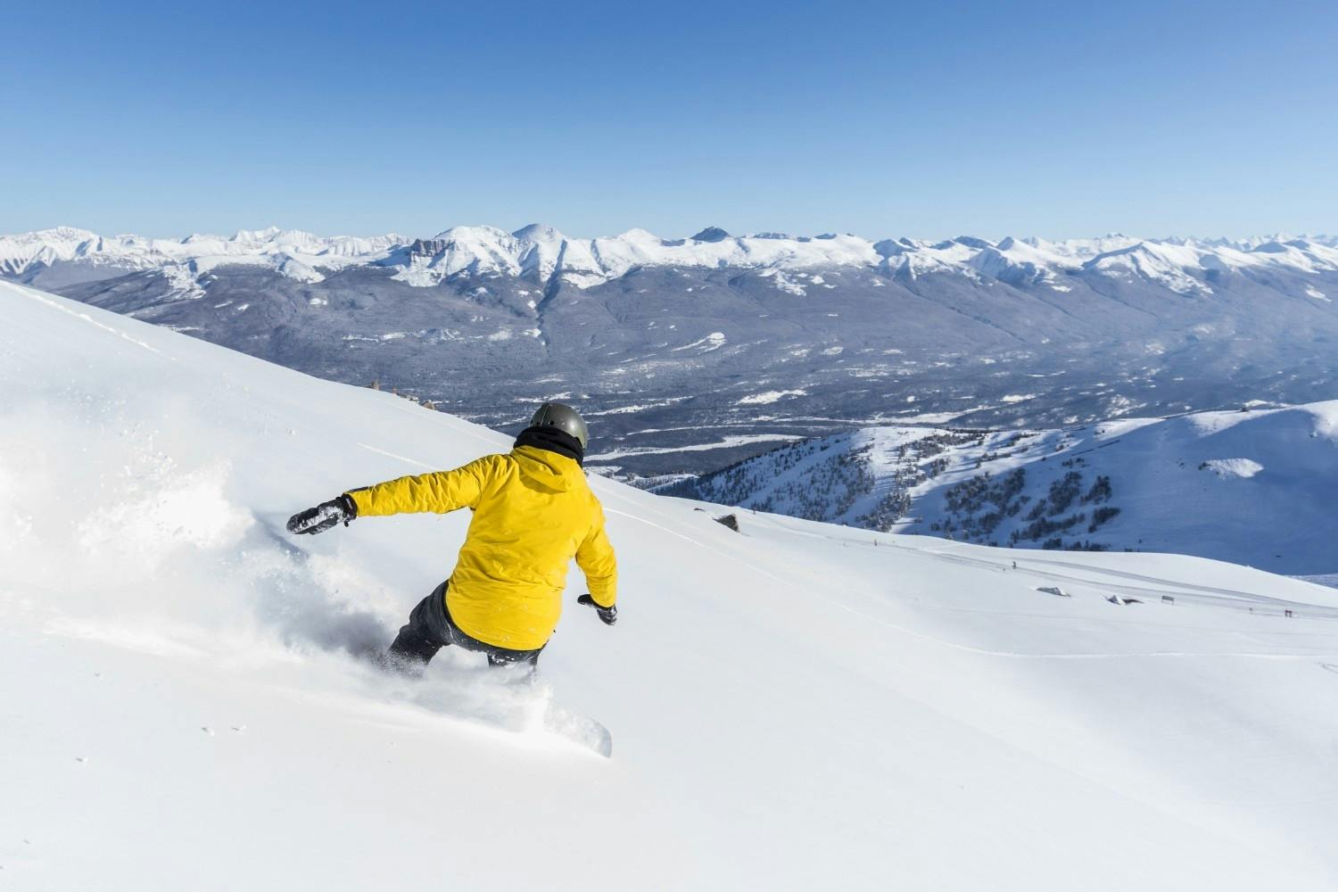 Snowboarder of undiscernible gender in yellow snowboarding jacket hitting the slopes at Echo Mountain near Denver in Colorado, USA.