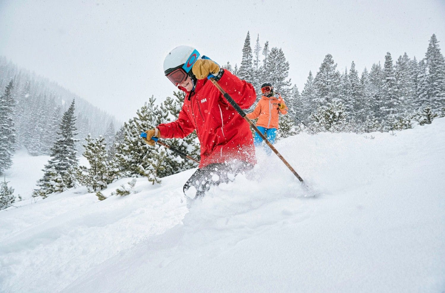 Two skiers of undiscernible gender in bright, colorful ski attire hitting the slopes at Breckenridge in Colorado, USA.