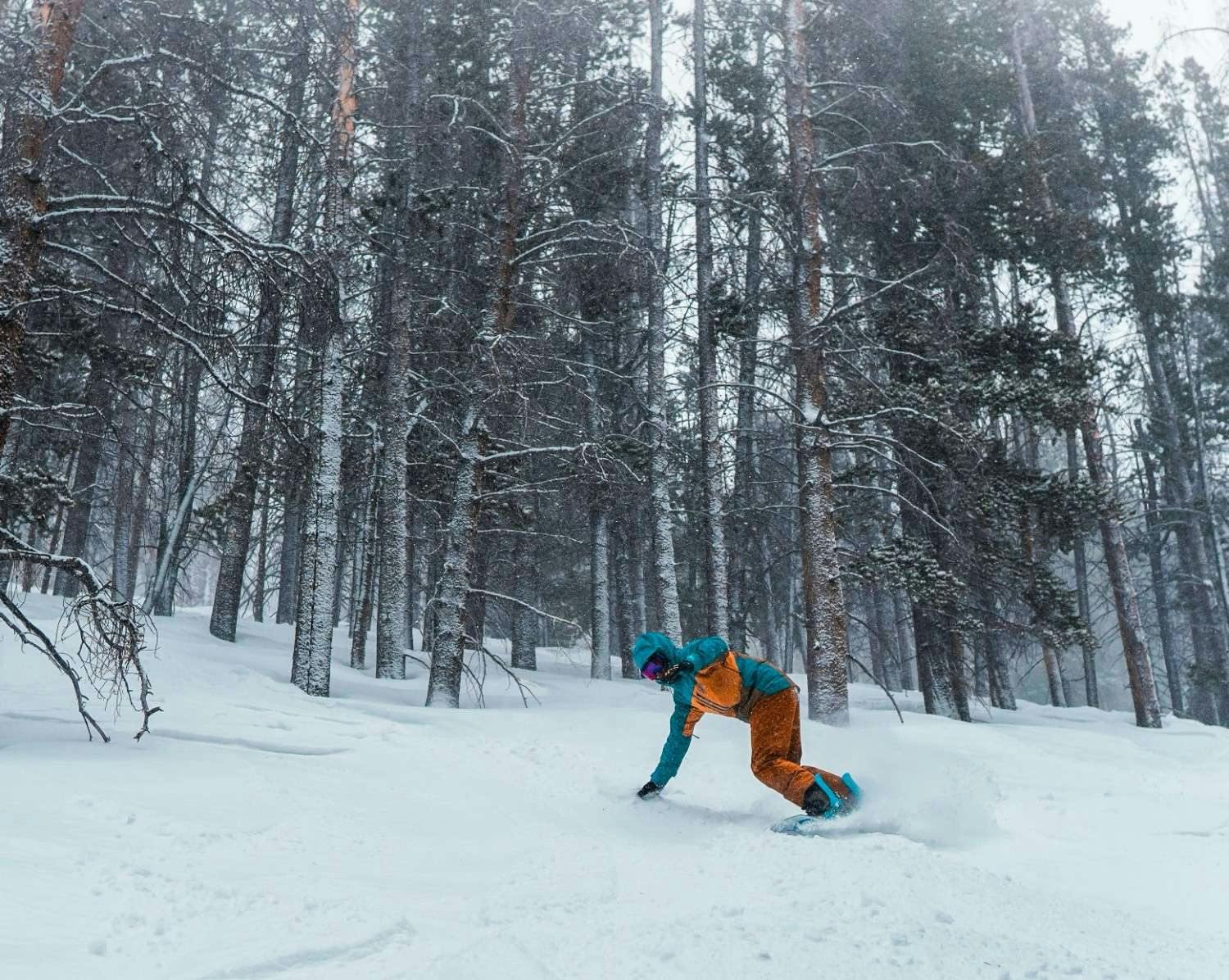 Snowboarder of undiscernible gender in teal and yellow ski attire hitting the slopes at Vail in Colorado, USA.