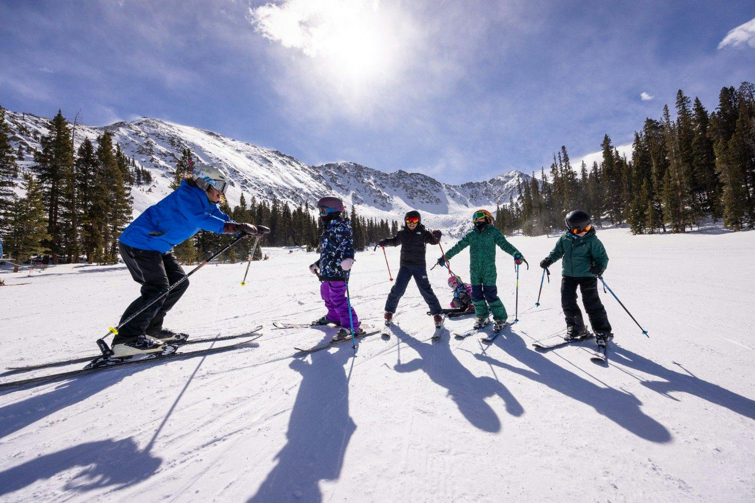 Arapahoe Basin ski instructor of undiscernible gender in blue ski jacket giving an afternoon lesson to a class of young skiers in colorful ski attire at Arapahoe Basin in Colorado, USA.