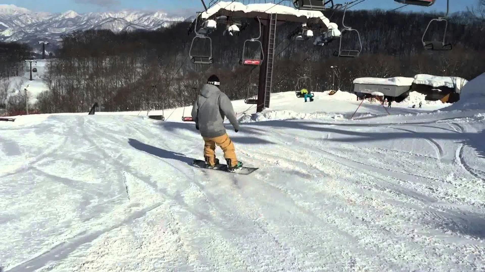 Male skier in yellow ski pants and grey ski jacket hitting the terrain park at Hakuba 47 & Goryu in Nagano, Japan.