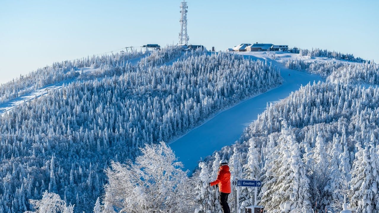 Skier of undiscernible gender in bright orange ski jacket gazing at the slopes of Mont Tremblant in Quebec, Canada.