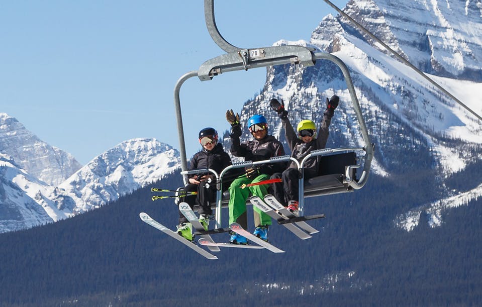 Three skiers in dark colored ski attire riding the chairlift at Lake Louise in Alberta, Canada.