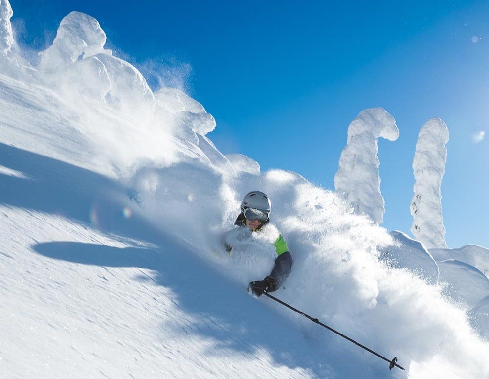 Skier of undiscernible gender in green and black ski attire hitting the slopes at Big White Ski Resort in British Columbia, Canada.