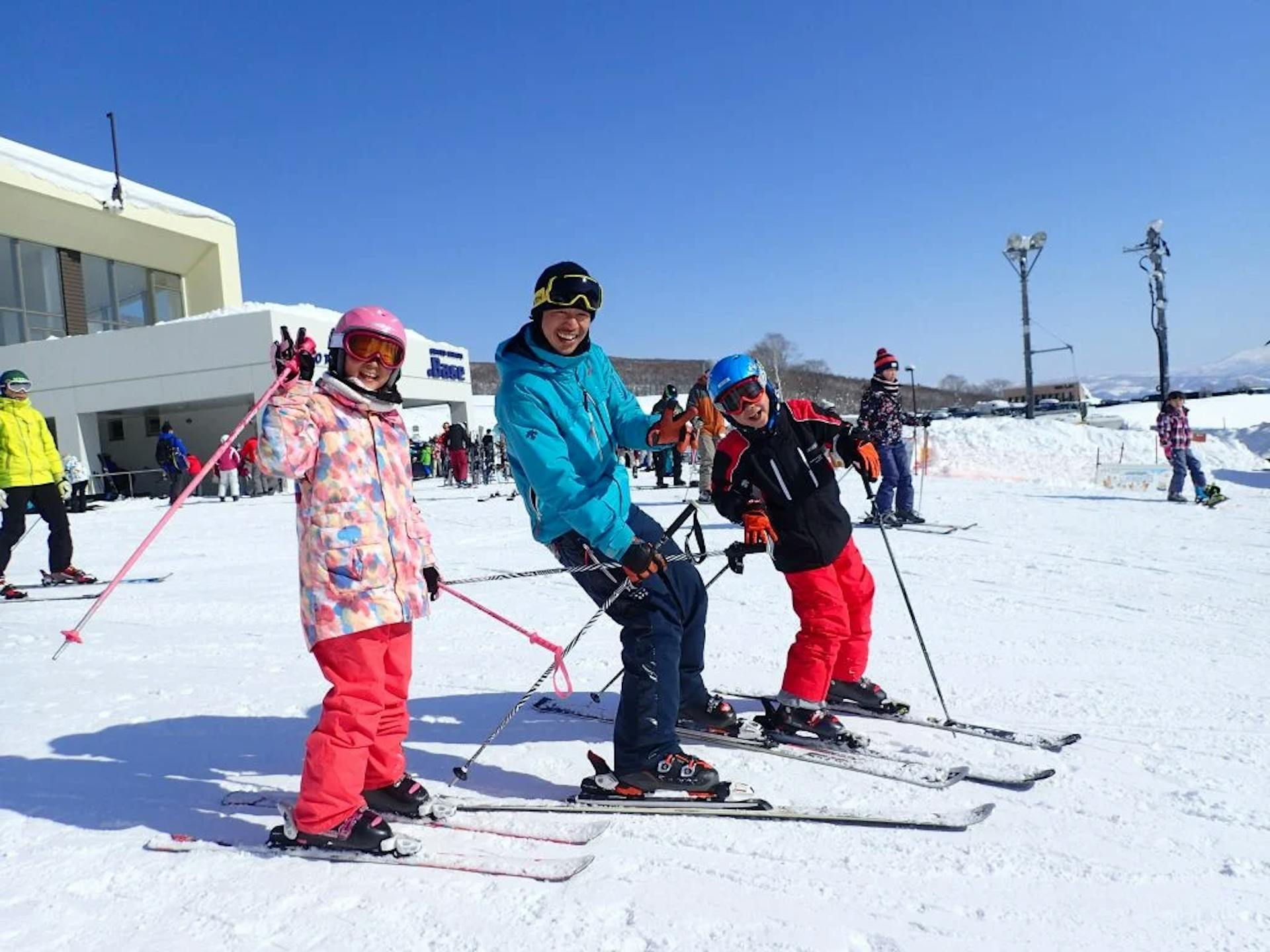 Male Niseko Ski Resort ski instructor in blue ski jacket giving a ski lesson to two young skiers in colorful ski attire at Niseko in Hokkaido, Japan.