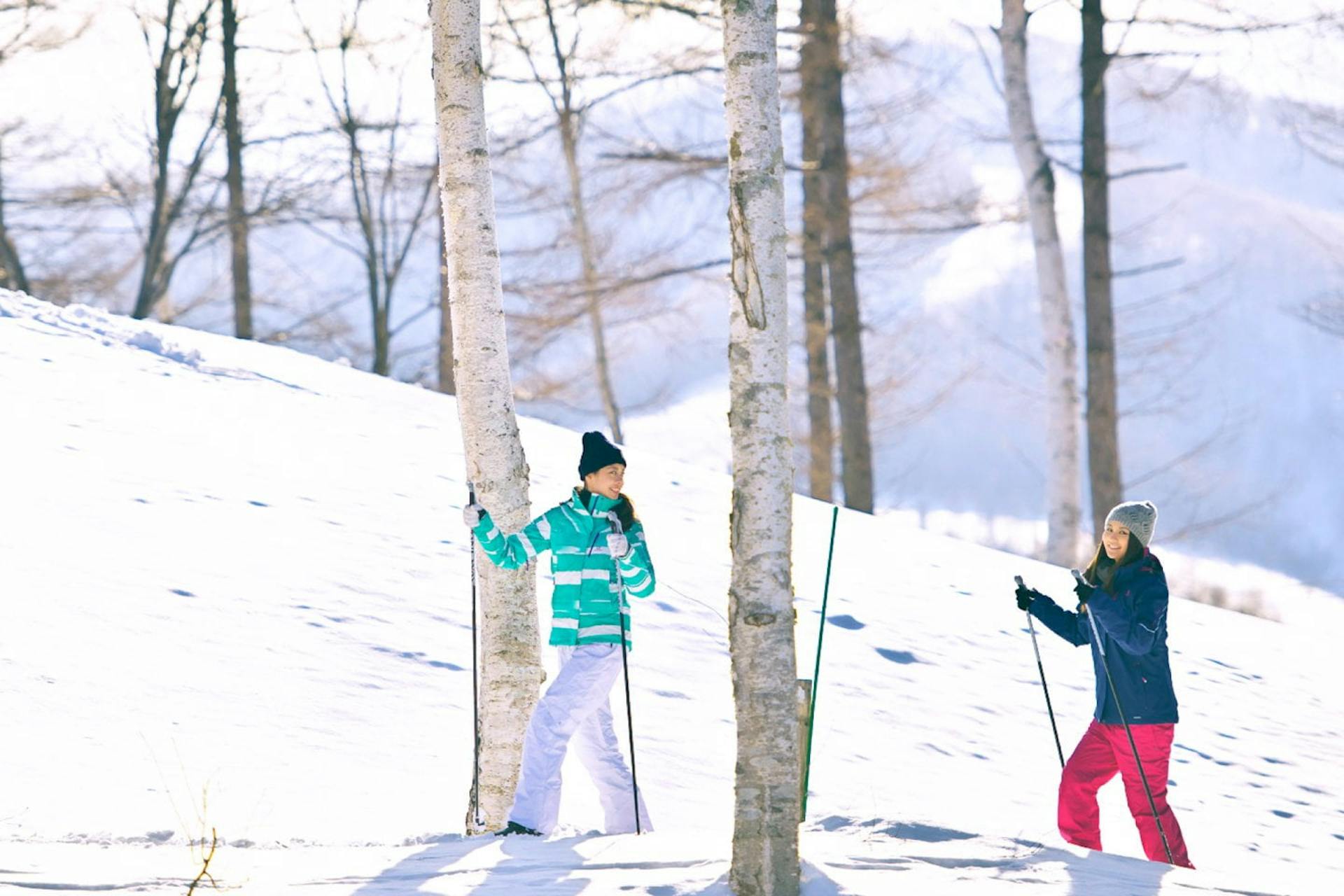 Two female skiers in brightly-colored ski attire enjoying a nature hike at Rusutsu in Hokkaido, Japan.