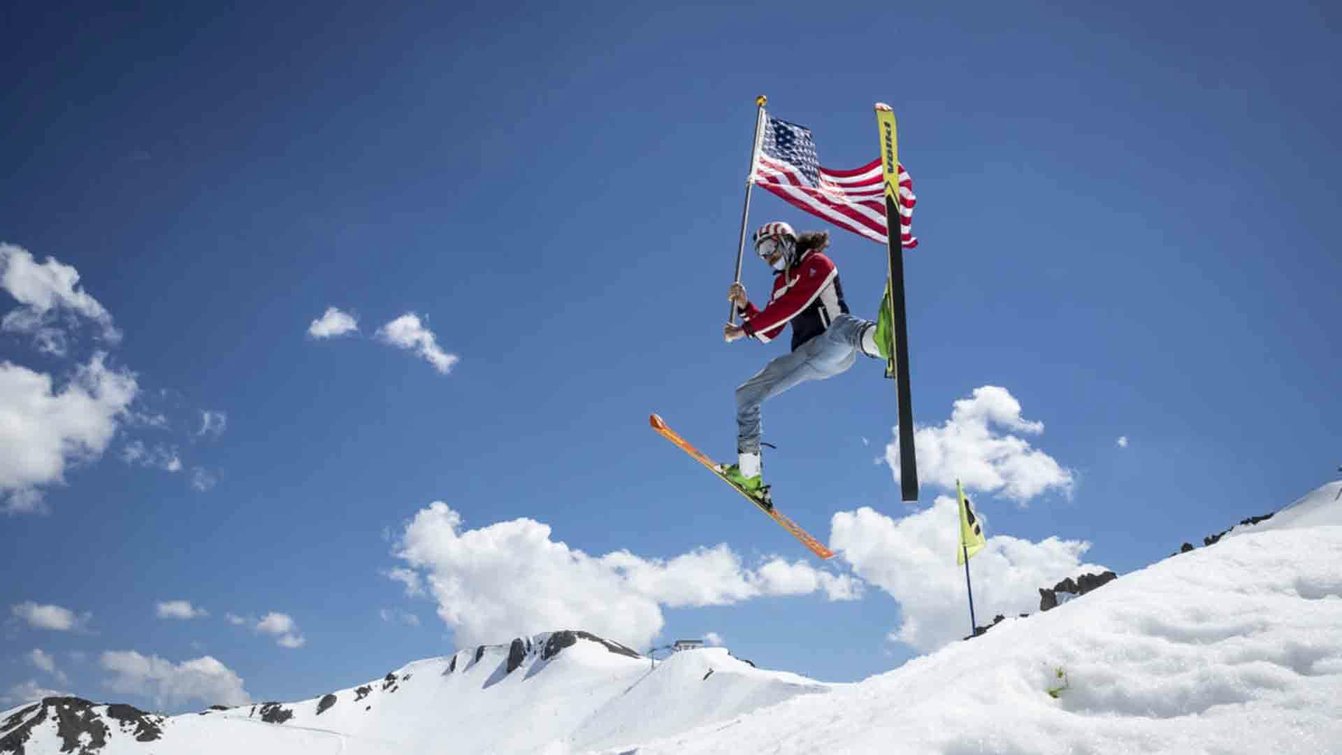 Female skier in red and blue ski jacket waving an American flag hitting the slopes during Freedom Fest at Palisades Tahoe (Squaw Valley) in California, USA.