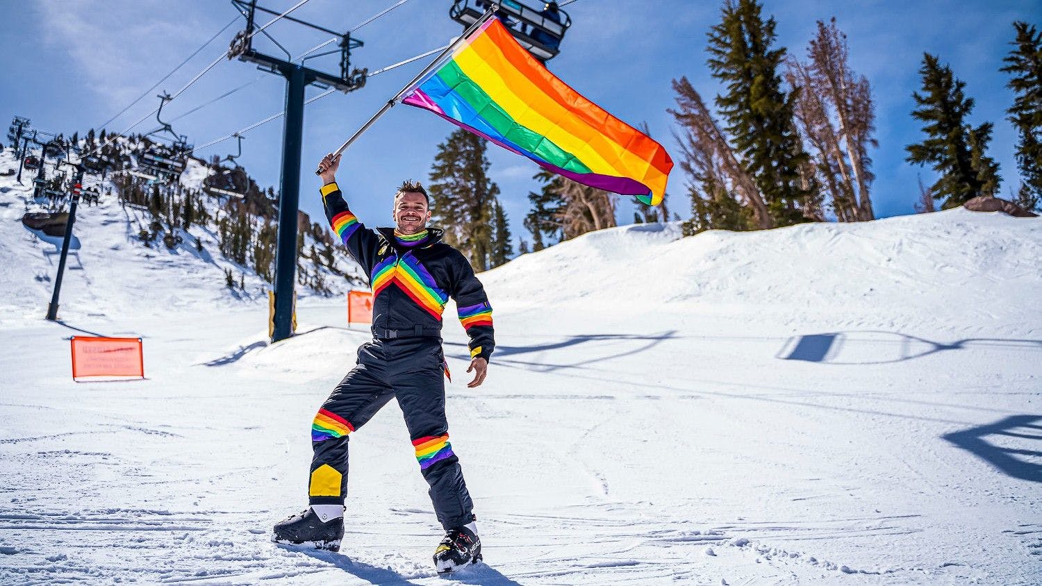 Male ice skier in rainbow-colored attire waving the LGBTQ+ community flag during the Elevation Ski Race event at Mammoth Mountain in California, USA.