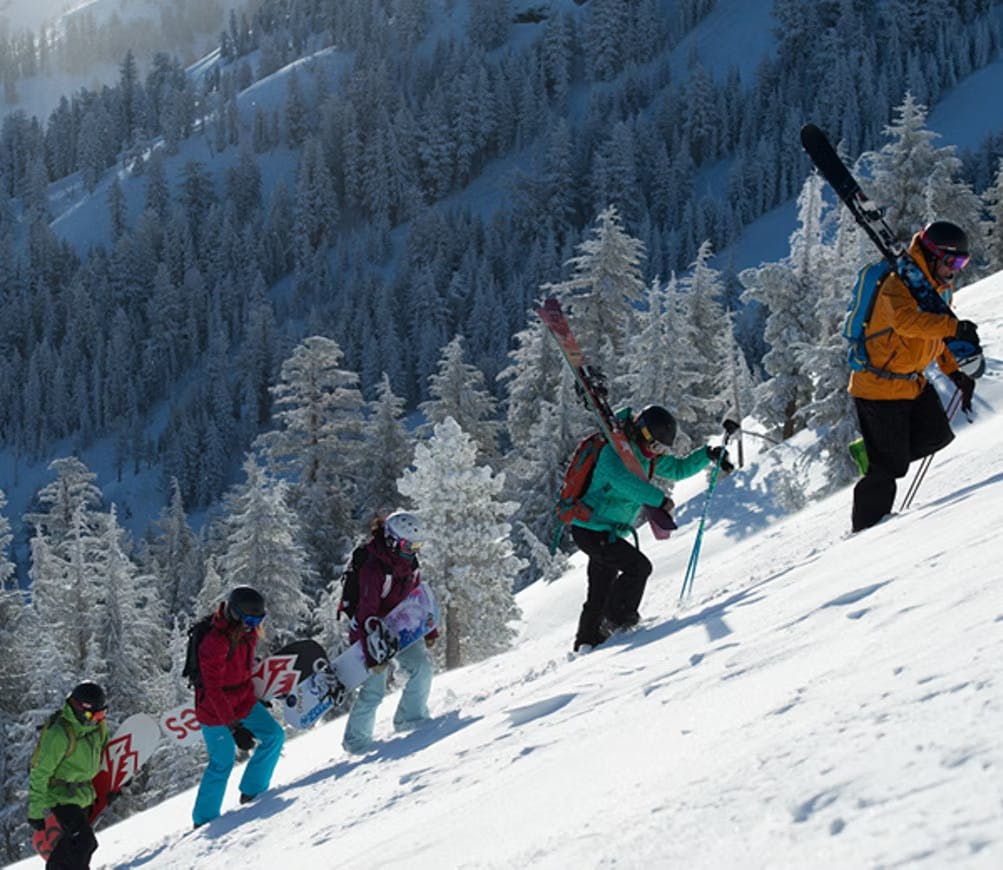 Five snowboarders in colorful snowboard attire uphilling to their next spot on the slopes of Kirkwood Mountain Resort in California, USA.