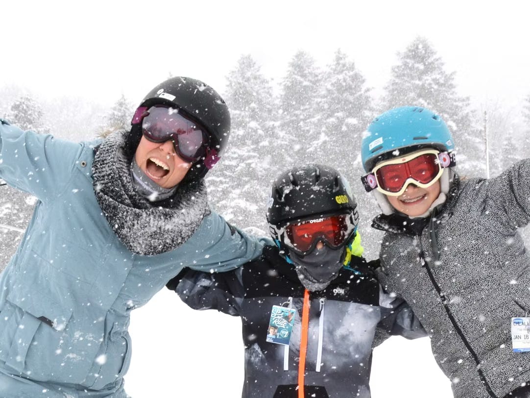 Male ski instructor in light blue ski jacket giving a ski lesson to two young skiers of indiscernible gender in gray-toned ski attire on the slopes at Seven Springs Mountain Resort near Washington, D.C., in the United States.