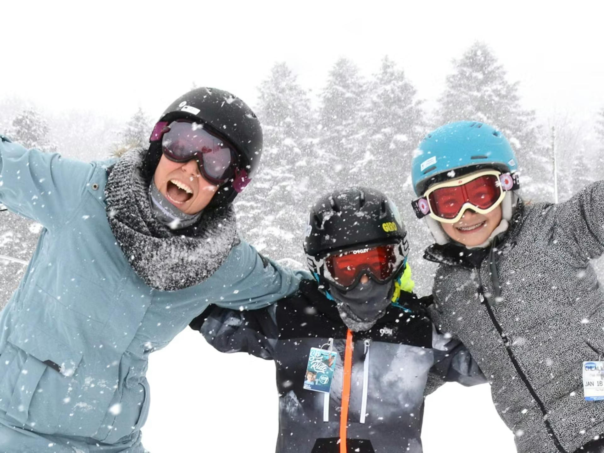 Male ski instructor in light blue ski jacket giving a ski lesson to two young skiers of indiscernible gender in gray-toned ski attire on the slopes at Seven Springs Mountain Resort near Washington, D.C., in the United States.