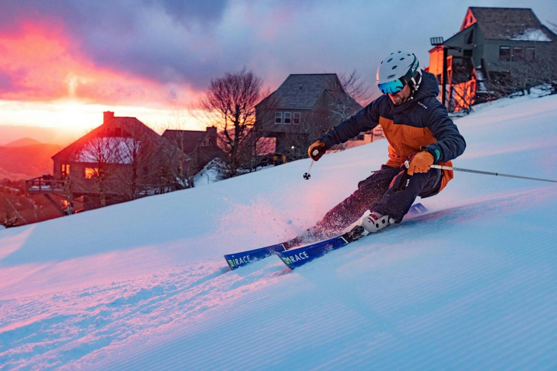 Male skier in orange and black ski attire hitting the slopes of Beech Mountain at twilight in North Carolina, USA.