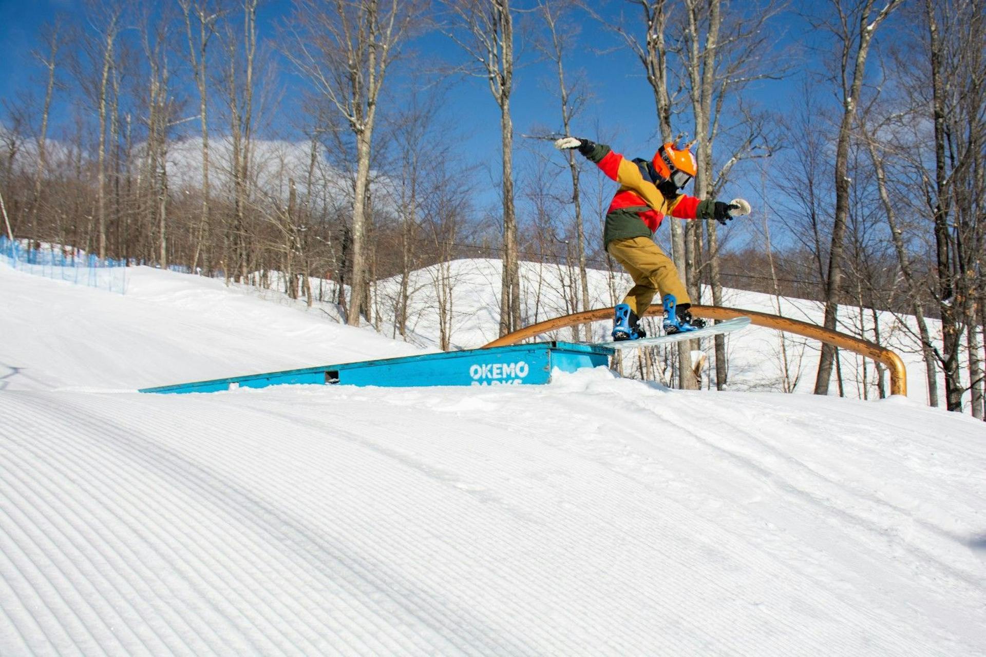 Snowboarder of undiscernible gender in brightly-colored snowboard attire hitting the terrain park at Stowe Mountain Resort in Vermont, USA.