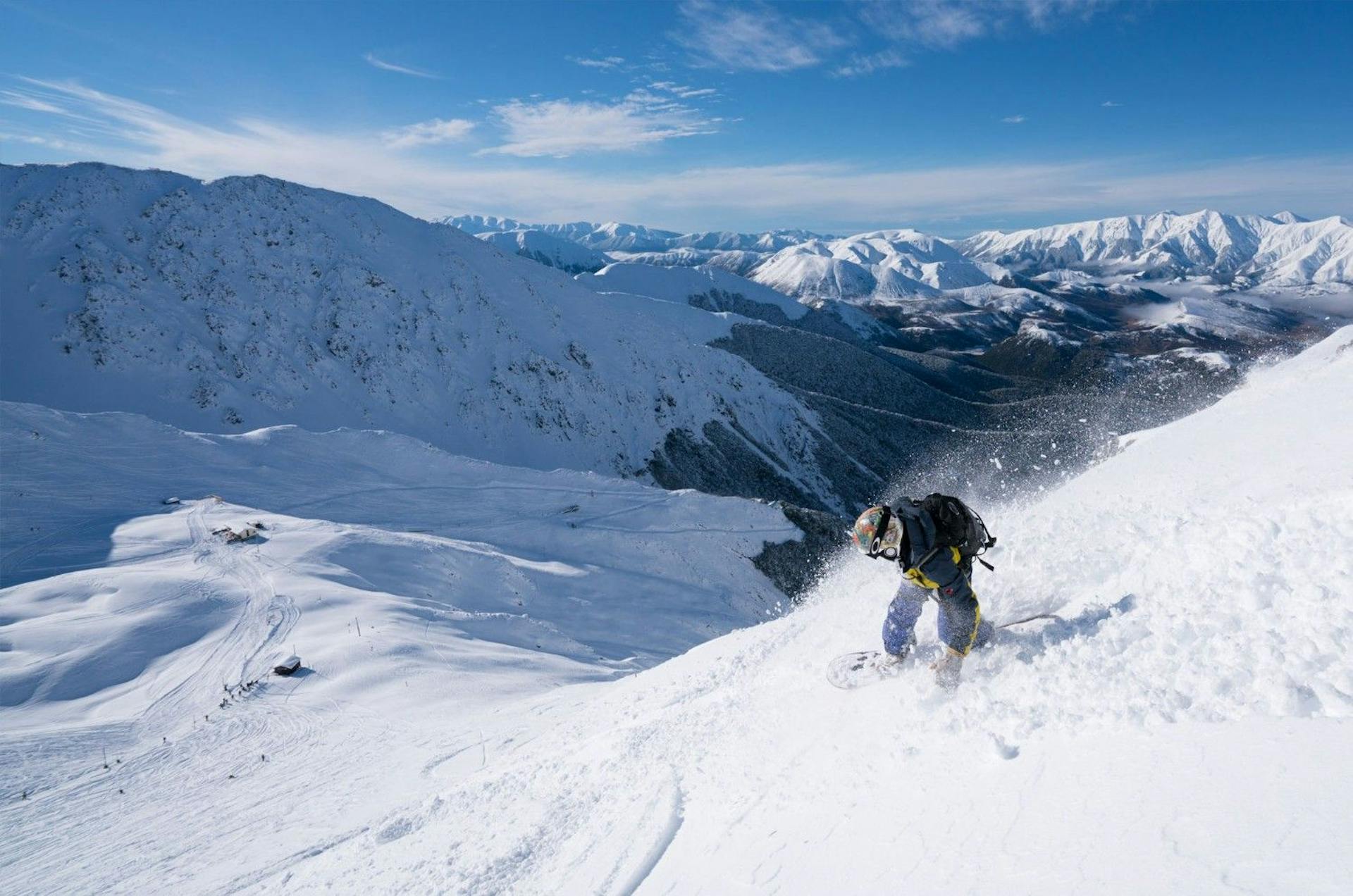 Snowboarder of undiscernible gender in dark-colored snowboard attire hitting the slopes at Broken River in New Zealand.