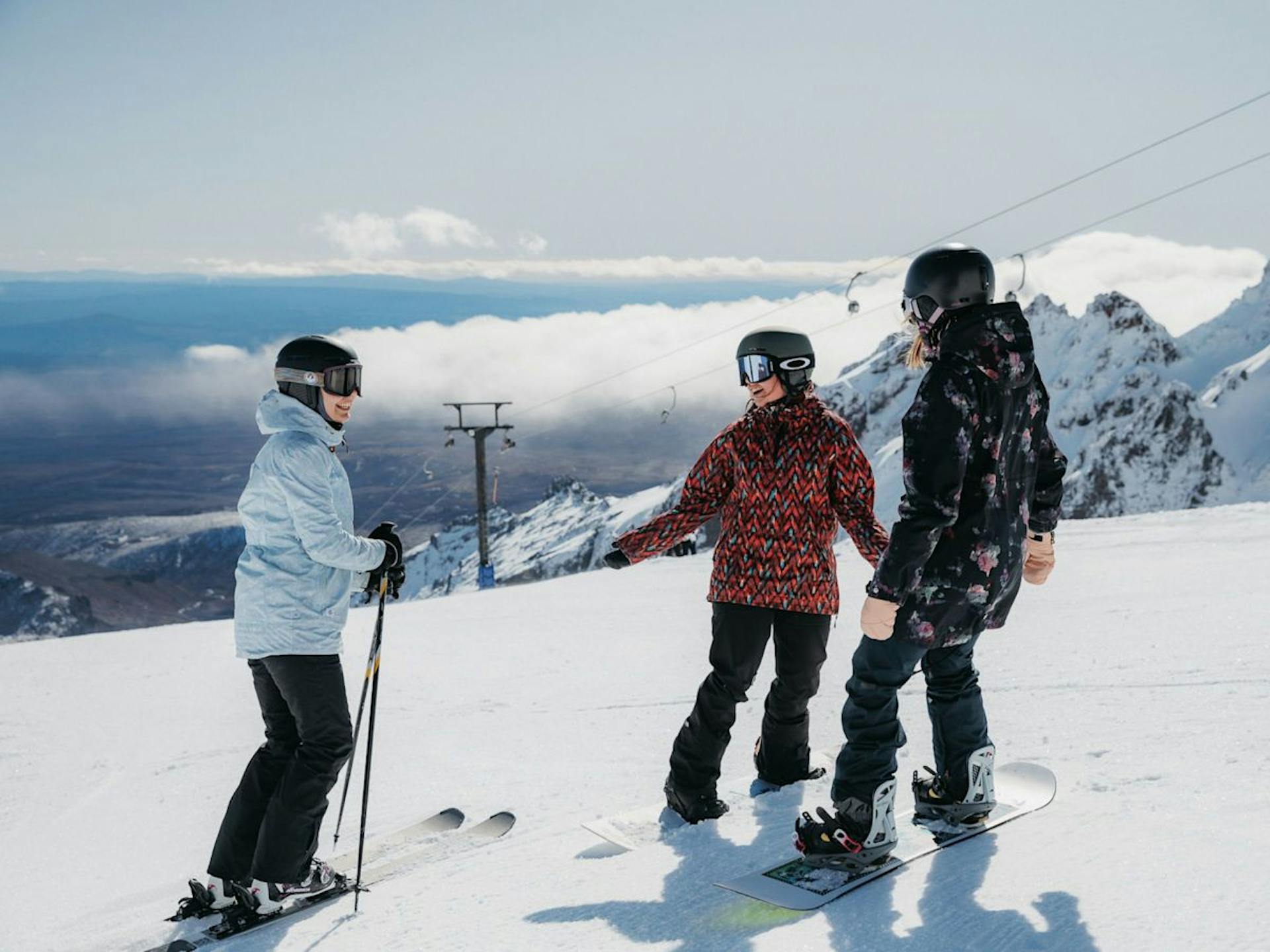 Diverse group of three skiers and snowboarders in colorful ski attire hitting the slopes at Whakapapa in New Zealand.