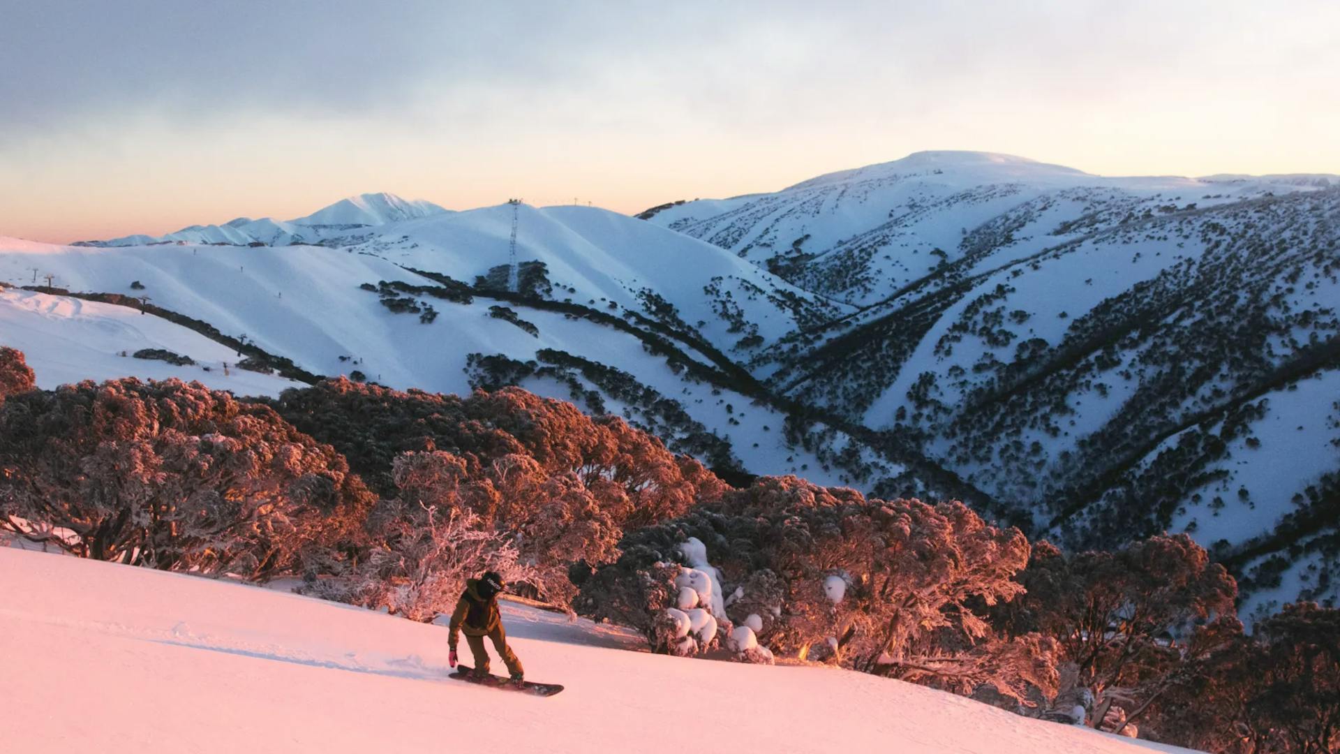 Snowboarder of undiscernible gender in dark-colored snowboard attire hitting the slopes at Mount Hotham in Australia.