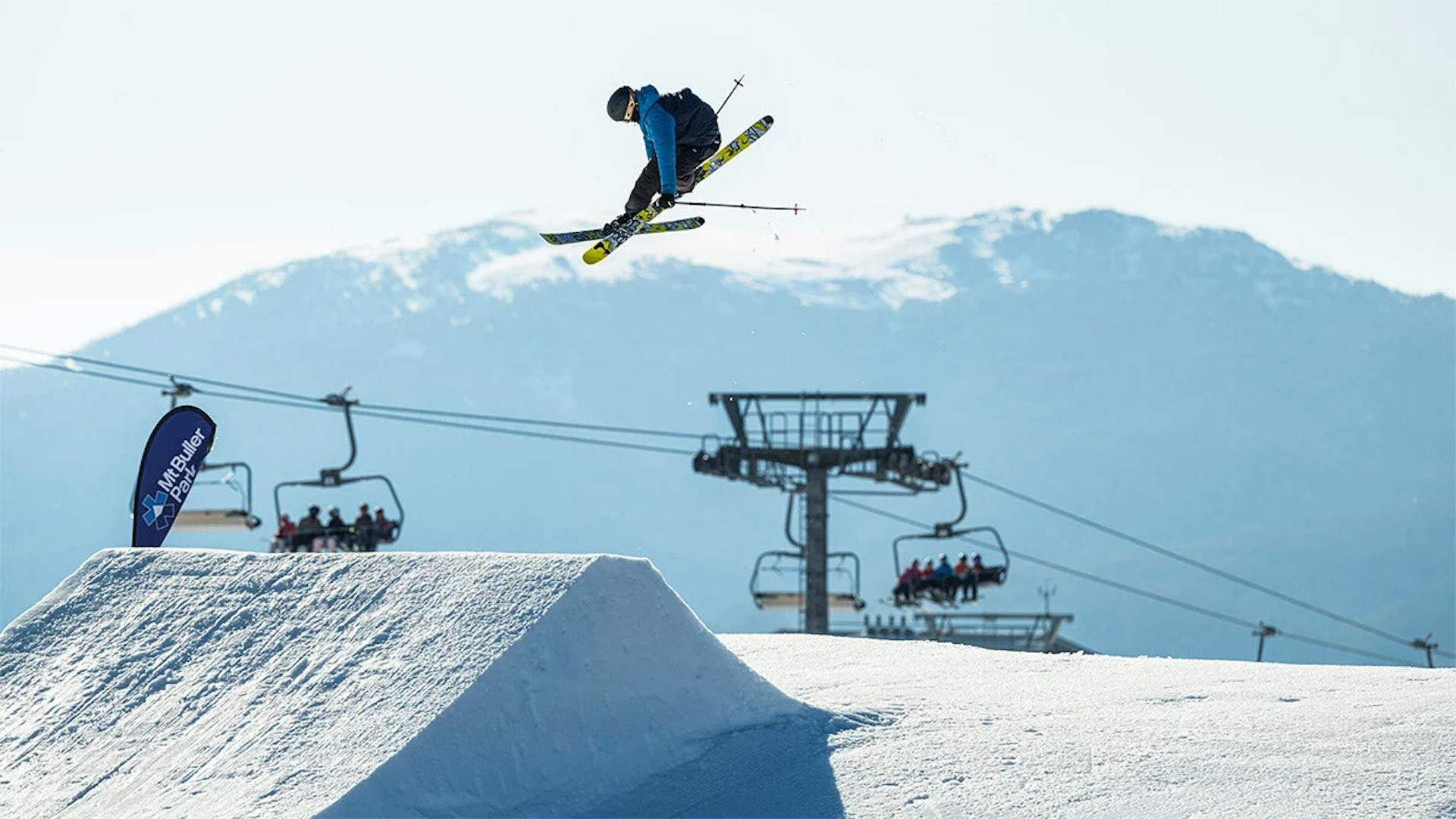 Skier of undiscernible gender in blue and black ski attire hitting the terrain park at Mount Buller in Australia.