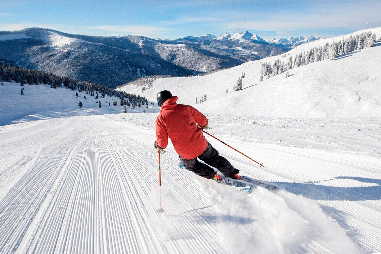Skier of undiscernible gender in orange ski jacket hitting the slopes at Vail Ski Resort in Colorado, USA.