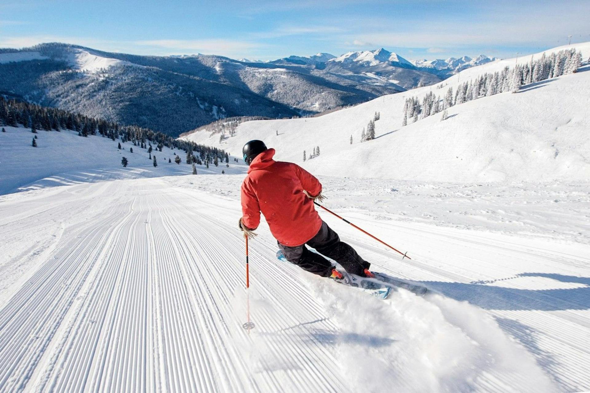 Skier of undiscernible gender in orange ski jacket hitting the slopes at Vail Ski Resort in Colorado, USA.