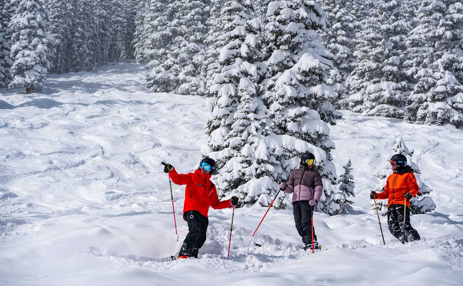 Three skiers of undiscernible gender in orange ski attire hitting the slopes at Aspen Snowmass in Colorado, USA.