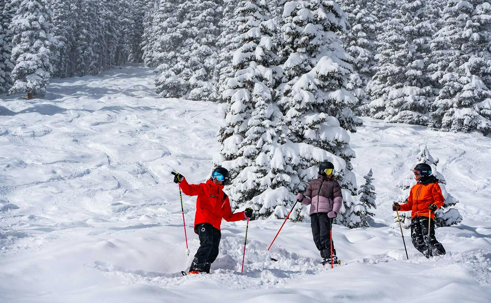 Three skiers of undiscernible gender in orange ski attire hitting the slopes at Aspen Snowmass in Colorado, USA.
