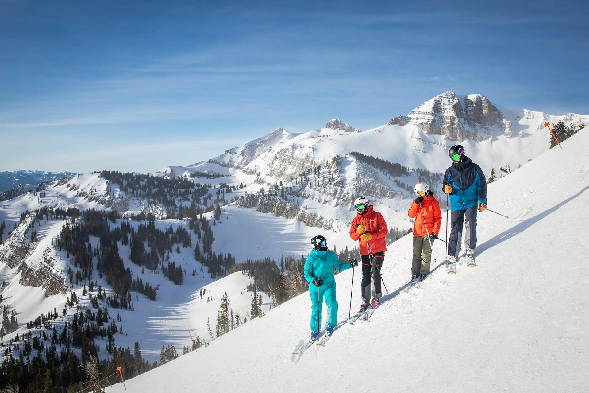 Four skiers of undiscernible gender in brightly-colored ski attire hitting the slopes at Jackson Hole in Wyoming, USA.