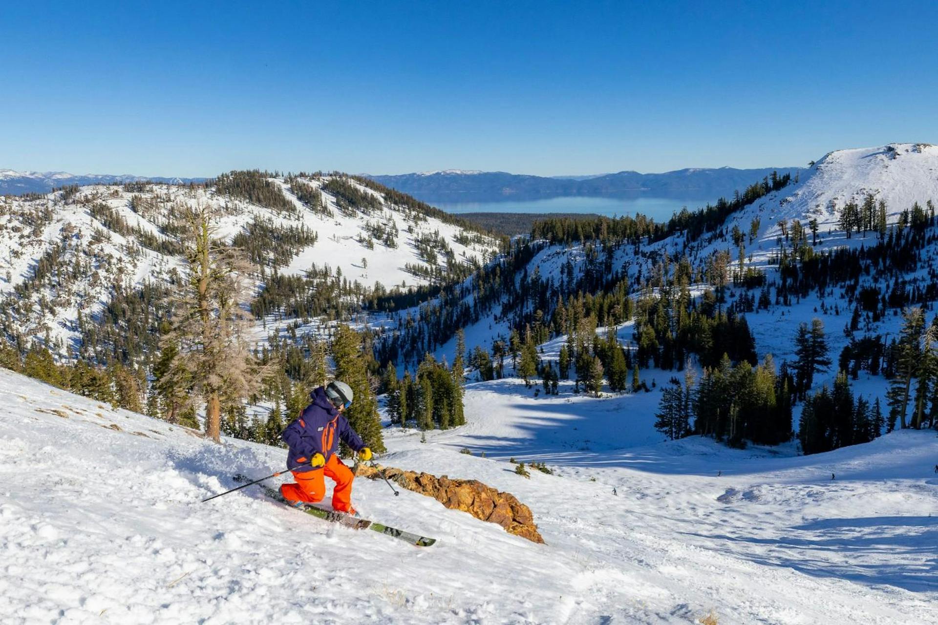 Skier of undiscernible gender in purple ski jacket and orange ski pants hitting the slopes at Palisades Tahoe (Squaw Valley) in California, USA.