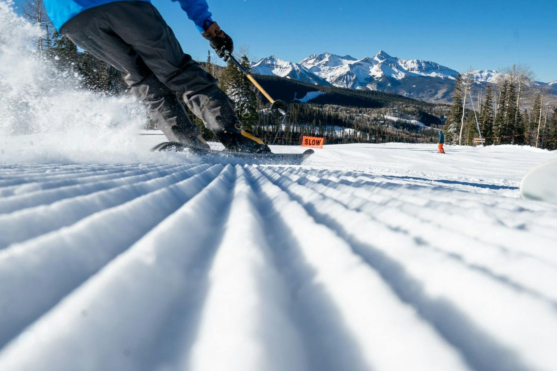 Close up of fresh corduroy and a skier of undiscernible gender in a blue ski jacket and black ski pants hitting the slopes at Telluride Ski Resort in Colorado, USA.