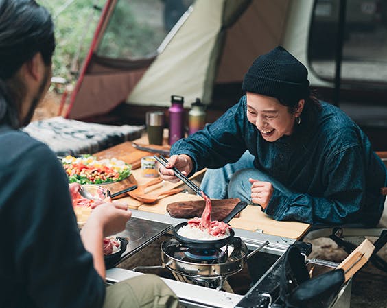 A photo of a happy person camping and picking up food with chop sticks.