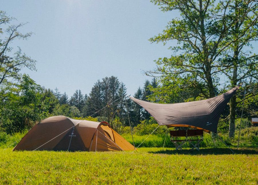 A brown tent and tarp in a green field in daytime