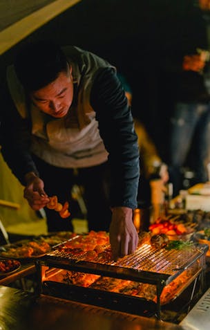 photo of a man arranging food on a low grill