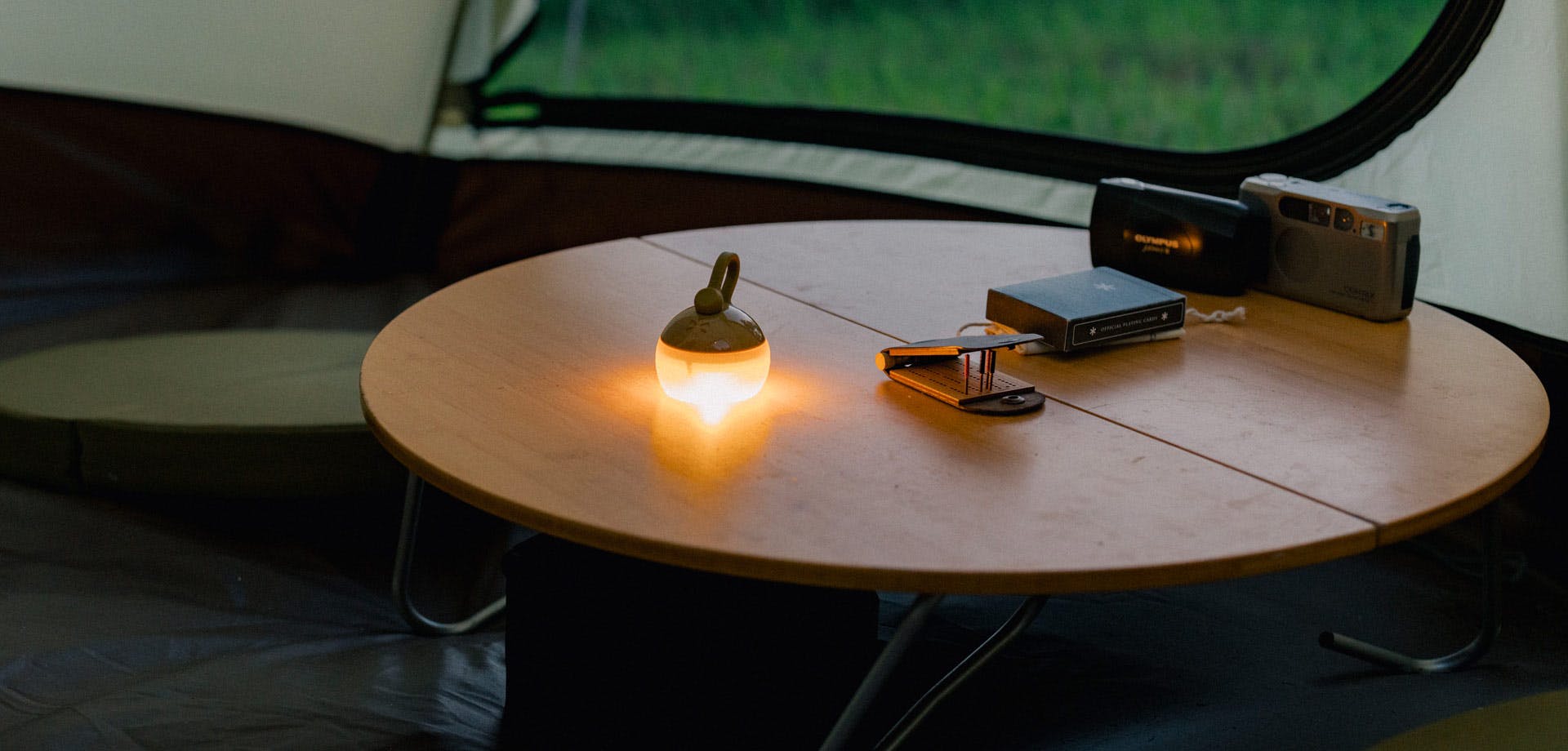 a photo of a round, low, wooden table with a small light and other personal items on it