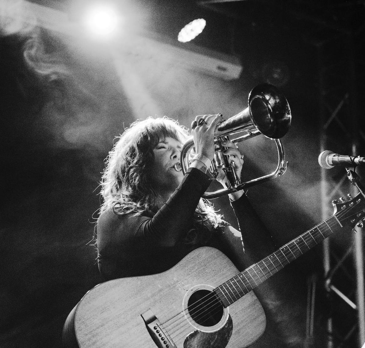 Carrie Jennings playing trumpet with guitar over her shoulder