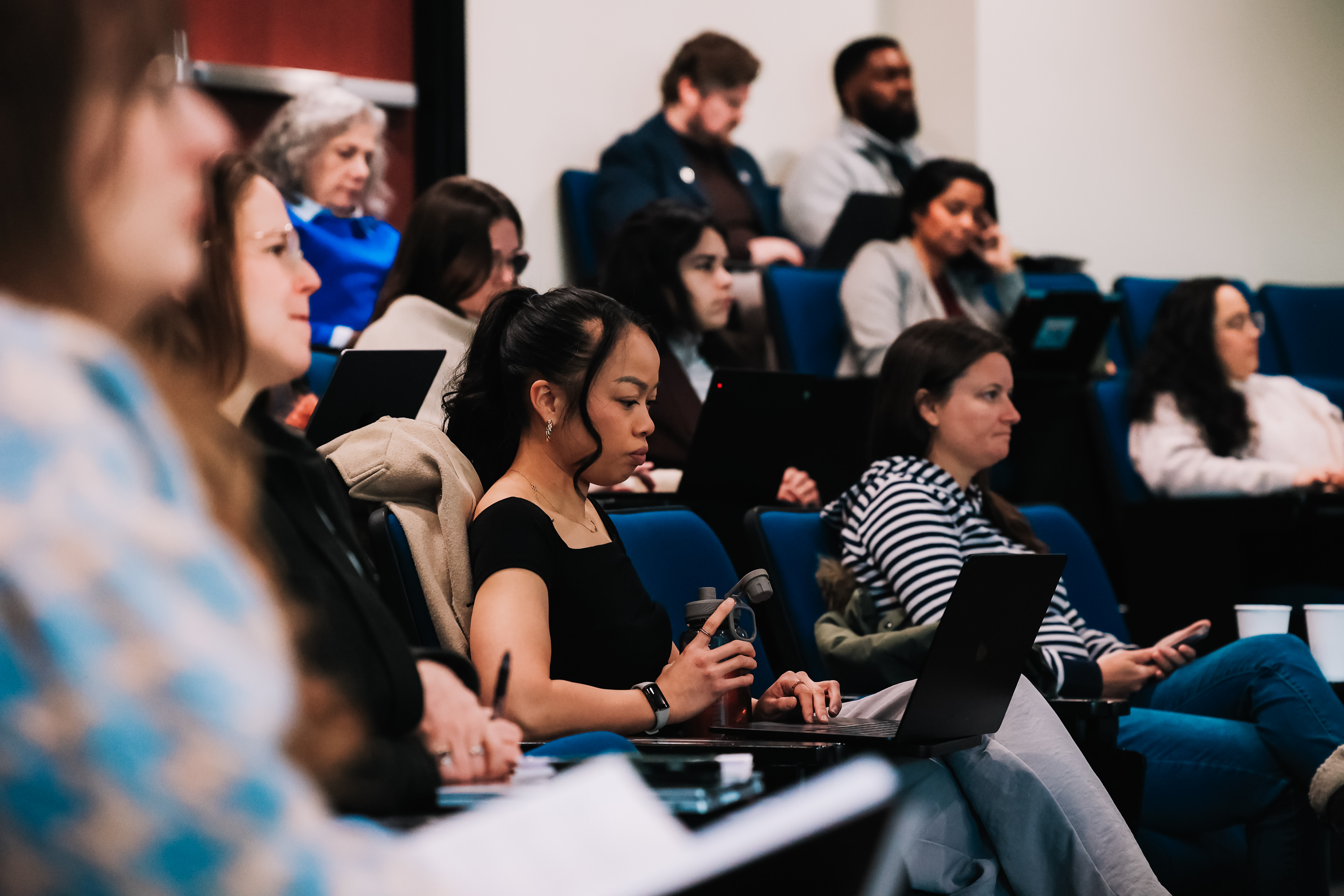 Attendees seated in a lecture-style room during a SocialNext conference session, taking notes on laptops and notebooks while focused on a presentation.