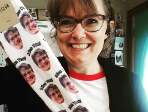 Woman smiling holding up a pair of custom socks with her face on them