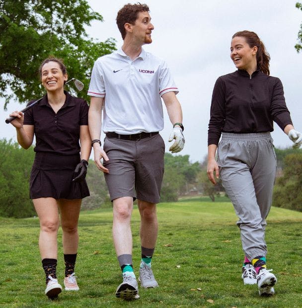 Three different people wearing branded socks and walking on a golf course