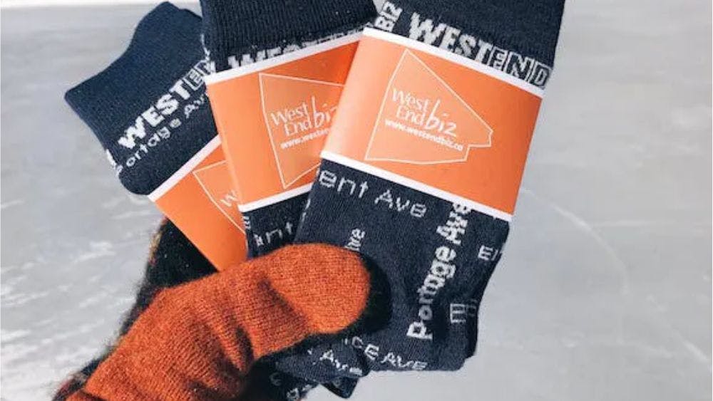 Orange gloved hand holding West End Biz custom logo socks with ice in background