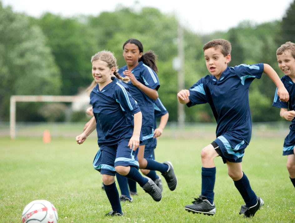 A children's soccer team playing on the field and chasing a ball with team soccer socks on