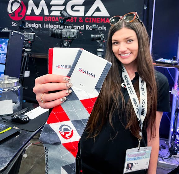 Person holding Omega Broadcast and Cinema argyle custom red and grey socks for trade show 