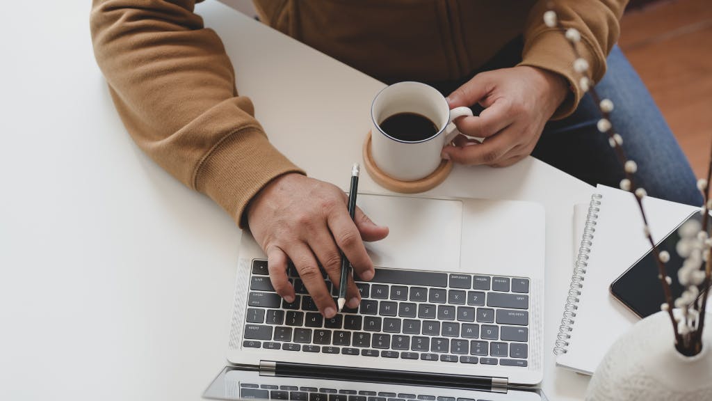 man working on laptop holding coffee mug