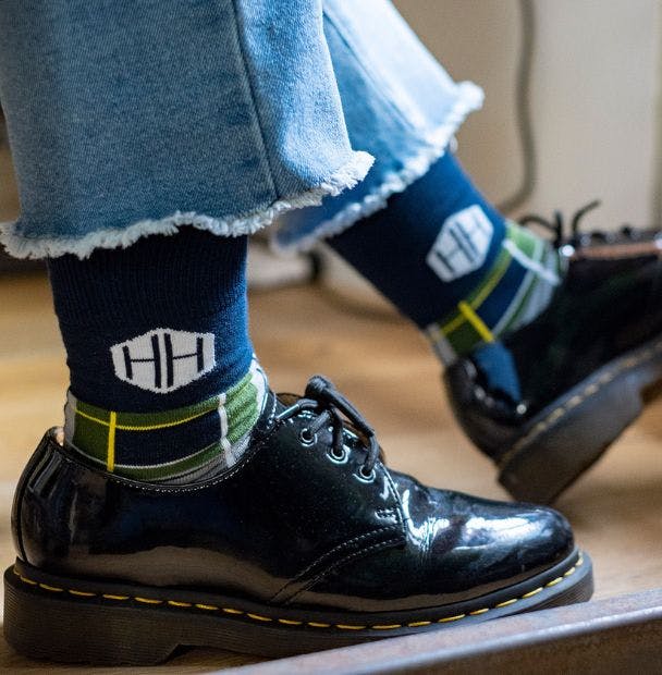Employee wearing custom low cost custom socks with an HH logo and plaid design, sitting at a desk