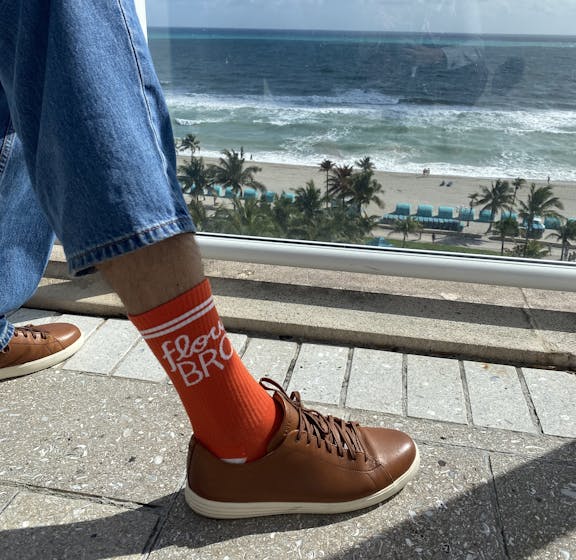 Person wearing orange Aunt Flow logo socks with beach in the background 