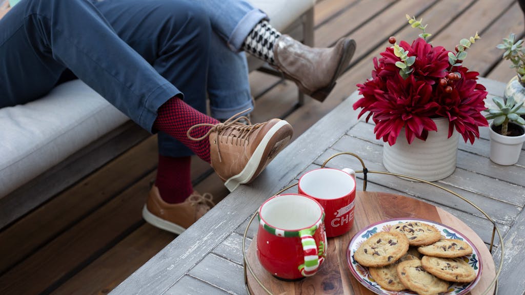 Two people wearing holiday socks with their feet on a table containing cookies and coffee